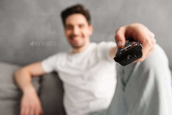 Blurry photo with focus on remote control, young man 30s in casu - Stock Photo - Images
