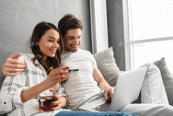 Lovely couple man and woman sitting on sofa in apartment near bi Stock Photo by vadymvdrobot