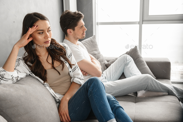 Photo of resentful guy and girl sitting together on couch at hom - Stock Photo - Images