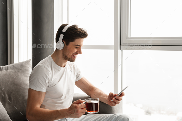 Photo in profile of smiling guy listening to music on cell phone Stock Photo by vadymvdrobot