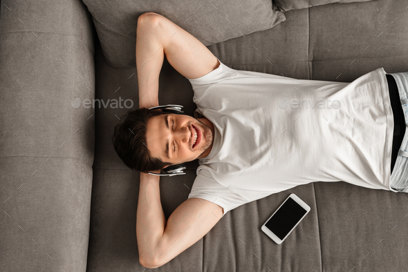 Photo from above of modern man 30s in white t-shirt lying on sof Stock Photo by vadymvdrobot