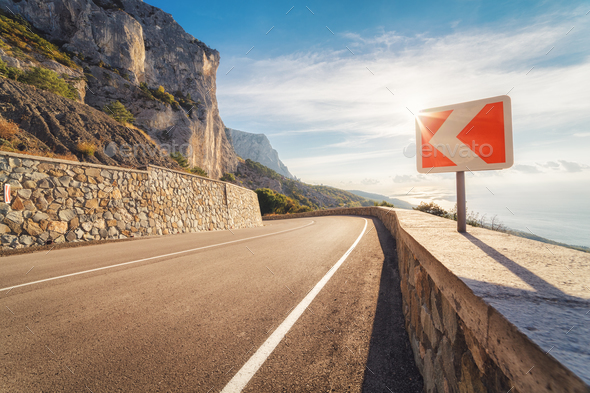 Asphalt road and road sign in mountains at sunset - Stock Photo - Images