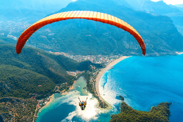 Paraglider tandem flying over the sea with blue water and mountains - Stock Photo - Images