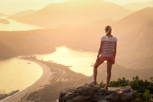 Landscape with woman, sea, mountain ridges and orange sky - Stock Photo - Images
