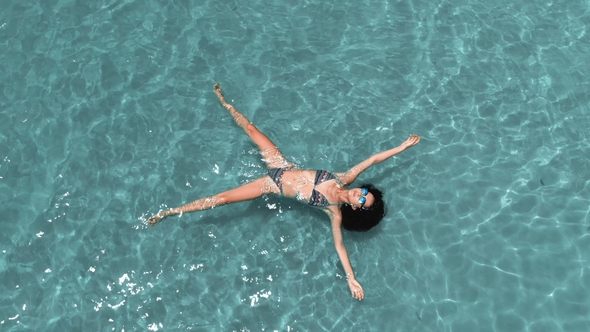 Beautiful Young Woman Floating in Crystal Clear Water, Aerial Rotating Shot alt