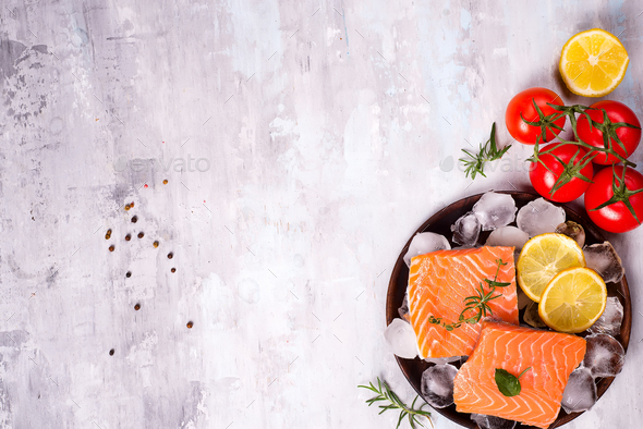 Salmon steaks on ice with lemon slice on wooden plate with tomato - Stock Photo - Images