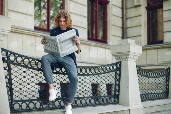 Young reddish man reading newspaper near old style building Stock Photo by arthurhidden