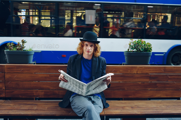 Red haired hipster man sitting on bench with newspaper - Stock Photo - Images