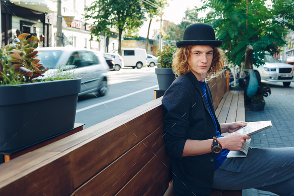 Red haired hipster man sitting on bench with newspaper - Stock Photo - Images