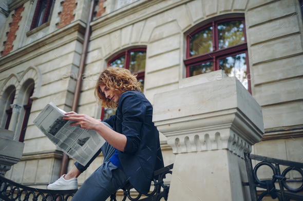 Young reddish man reading newspaper near old style building - Stock Photo - Images