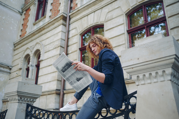 Young reddish man reading newspaper near old style building - Stock Photo - Images