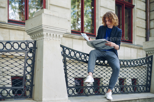 Young reddish man reading newspaper near old style building - Stock Photo - Images
