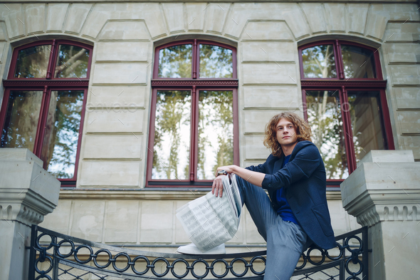 Young reddish man reading newspaper near old style building - Stock Photo - Images