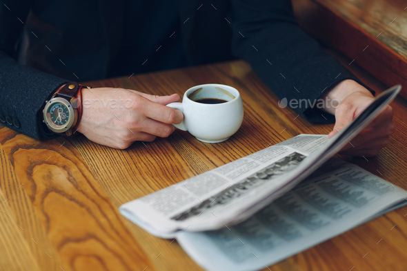 Man's hands close-up holding cup of coffee and a newspaper - Stock Photo - Images