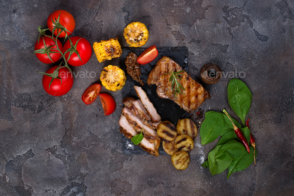 sliced pork steak and grilled vegetables on slate board on stone table. - Stock Photo - Images
