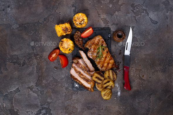 sliced pork steak and grilled vegetables on slate board on stone table. - Stock Photo - Images