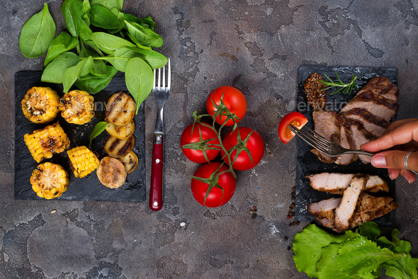 female hand holds a fork with slice tomato on the background fresh three types of grilled steak - Stock Photo - Images
