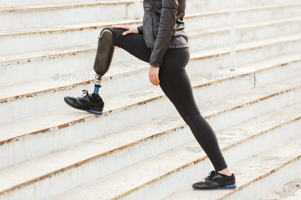 Sportswoman with prosthetic leg smiling while using mobile phone sitting on  steps stock photo