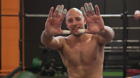 Fitness Man Smiling and Showing Palms with Bloody Calluses in Gym