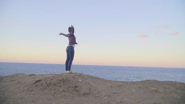 Young Woman Standing on Top of a Mountain and Looking at the Sea, Sunset