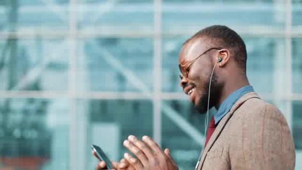 African American Businessman in the Sunglasses Talking on the Phone with Headphones Near the Office alt