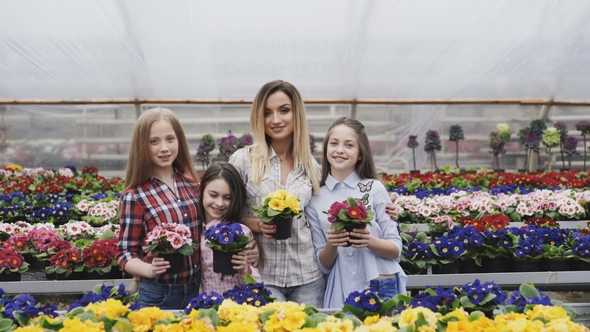 Portrait of Smiling Four Girls Stretching Synchronously Flower Pots To Camera