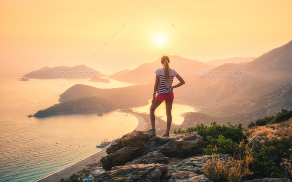 Landscape with woman, sea, mountain ridges and orange sky - Stock Photo - Images