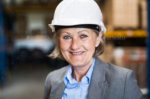 Senior woman warehouse manager or supervisor with white helmet. Stock Photo by halfpoint