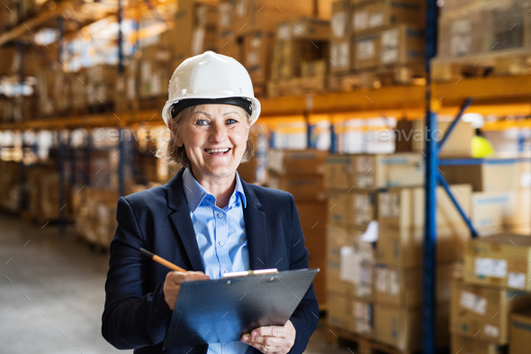 Senior woman warehouse manager or supervisor with white helmet and clipboard. - Stock Photo - Images
