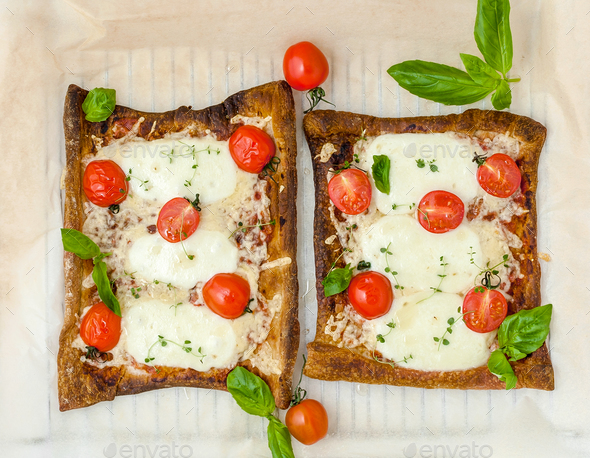 Two homemade rectangular pizzas with tomatoes, mozzarella and ba