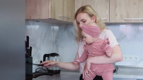Mother Prepares Food Holding Baby in Her Arms alt