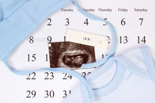 Pregnancy test, ultrasound scan of baby and blue clothing for newborn on calendar - Stock Photo - Images