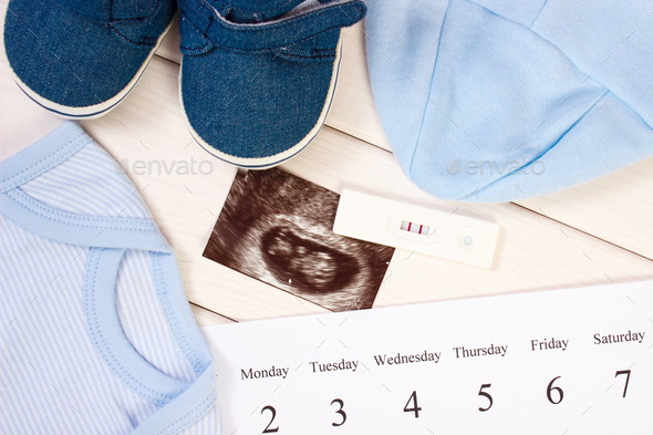 Pregnancy test, ultrasound scan of baby, blue clothing for newborn and calendar - Stock Photo - Images