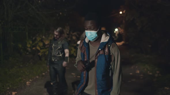 Young Afro Man in Safety Mask Walking on Dark Road Followed By Infected Monster alt