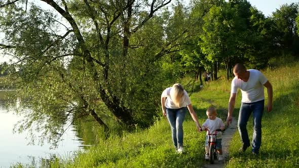 Happy family teaches their son to ride a bike outdoors and smiles. alt