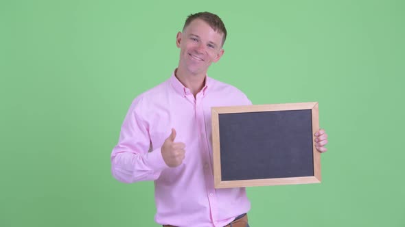 Portrait of Happy Businessman Holding Blackboard and Giving Thumbs Up alt
