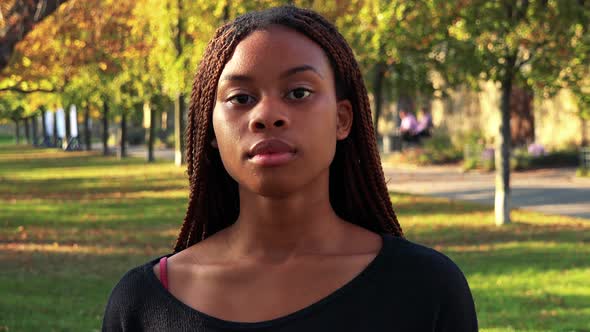 Young Beautiful Black Woman Looks To Camera with Serious Face in the Park alt