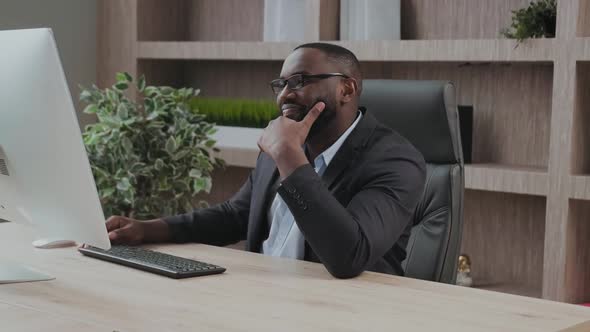 Goodlooking African American Office Emplyee Looks Delighted and Satisfied at His Computer Screen alt