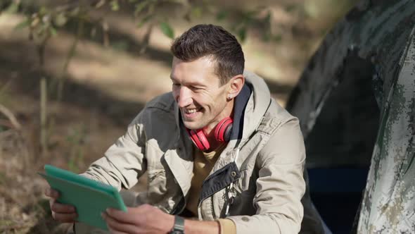 Cheerful Man Laughing Watching Video Online on Tablet Sitting at Tree on Forest alt