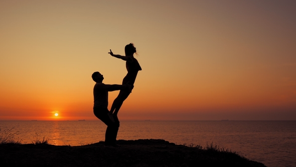 Amazing Silhouettes of Beautiful Couple Doing Acrobatic Yoga on the Sea or Ocean Beach at Sunrise alt