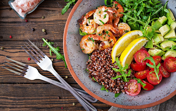Delicious healthy Buddha bowl with shrimps, tomato, avocado, quinoa, lemon and arugula - Stock Photo - Images
