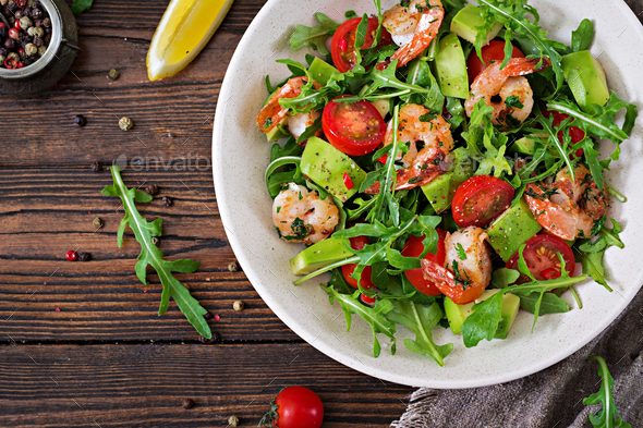 Fresh salad bowl with shrimp, tomato, avocado and arugula on wooden background close up. - Stock Photo - Images