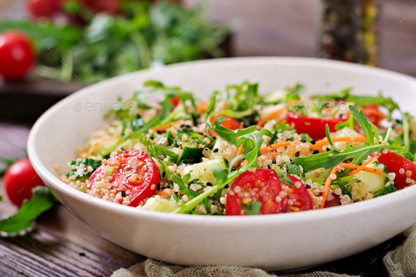 Salads with quinoa, arugula, radish, tomatoes and cucumber in bowl on wooden background - Stock Photo - Images