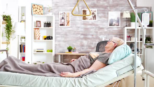 Retired Disabled Lady Lying in Hospital Bed in Cozy and Bright Room in Retirement Home alt