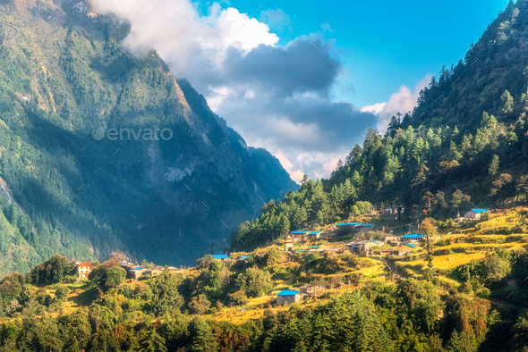Small village on the hill lighted by a sunbeam against mountains - Stock Photo - Images