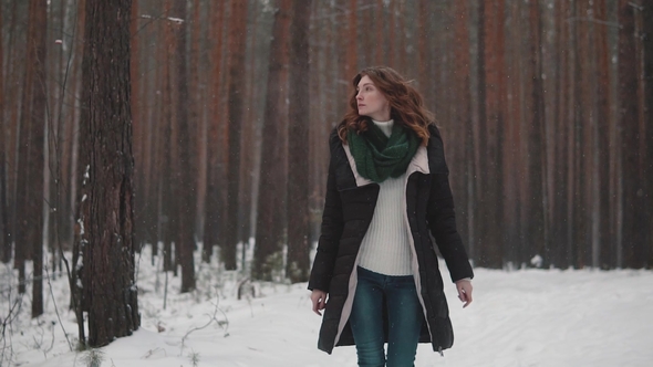 Red-haired Girl Strolls Through the Winter Forest Under a Snowfall. alt