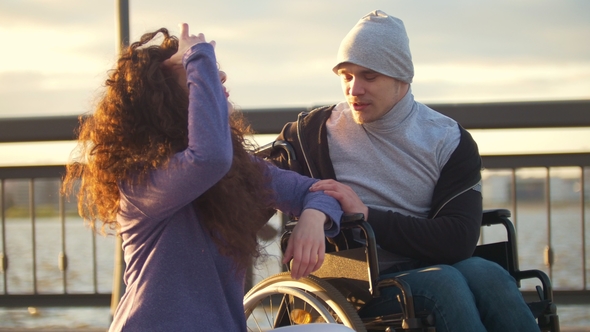 Happy Couple Disabled Man in Wheelchair Talking with Young Woman Enjoying the Sunset alt