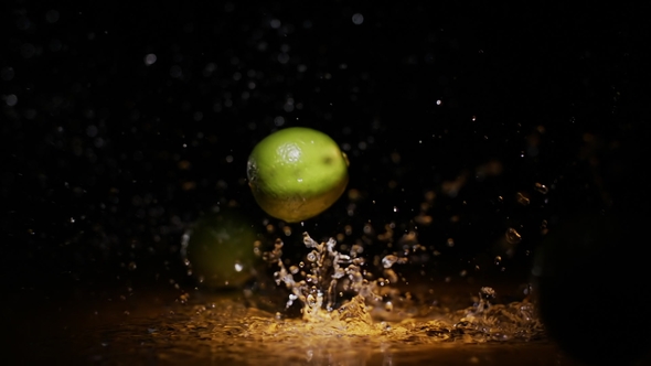 Citrus Limes Falling on Wet Surface in Orange Light Spot and Black Background alt