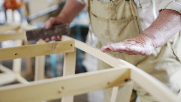 Elderly Man Carpenter Builds a Small Boat with His Hands Out of Wood in a Small Workshop alt