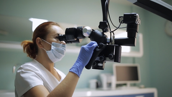 Female Dentist with Dental Tools - Microscope, Mirror and Probe Treating Patient Teeth at Dental